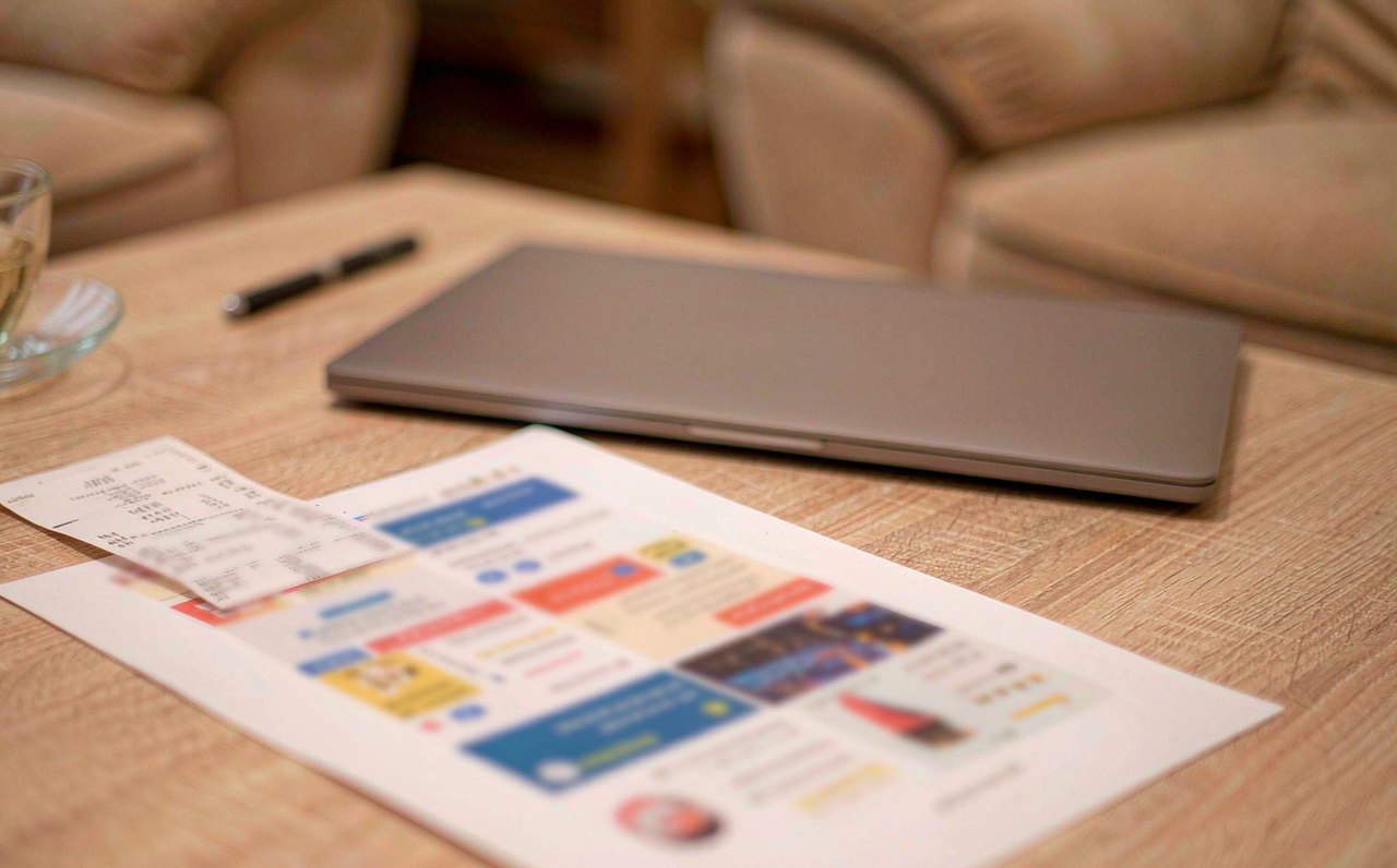 A store credit card receipt and a financing offer flyer resting on a kitchen table next to a closed laptop and a pen