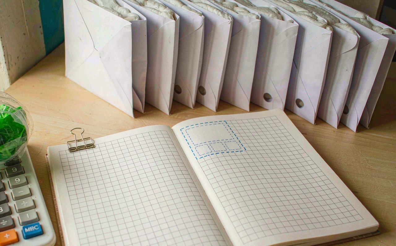 A kitchen table with an open budgeting notebook, a calculator, and labeled white envelopes arranged in a neat row