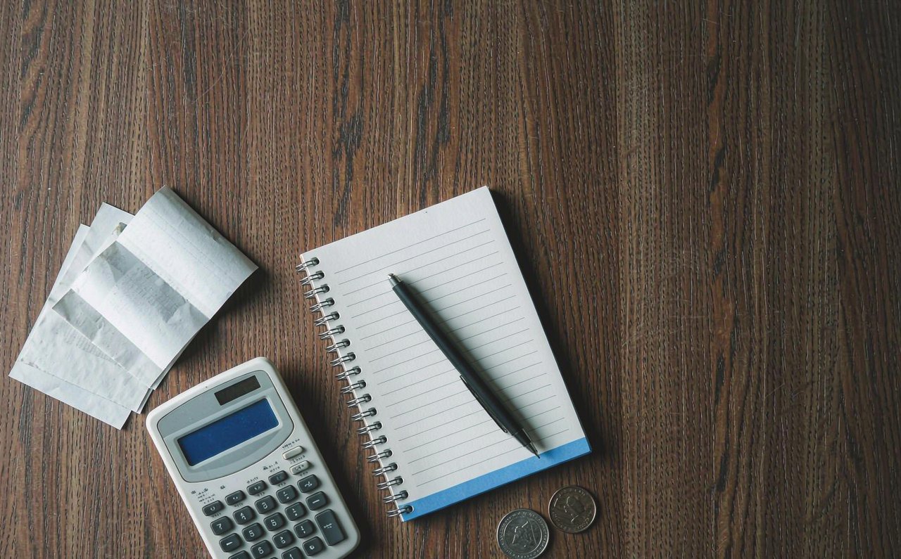 An overhead view of a calculator, receipts, and a notepad on a dark wooden desk