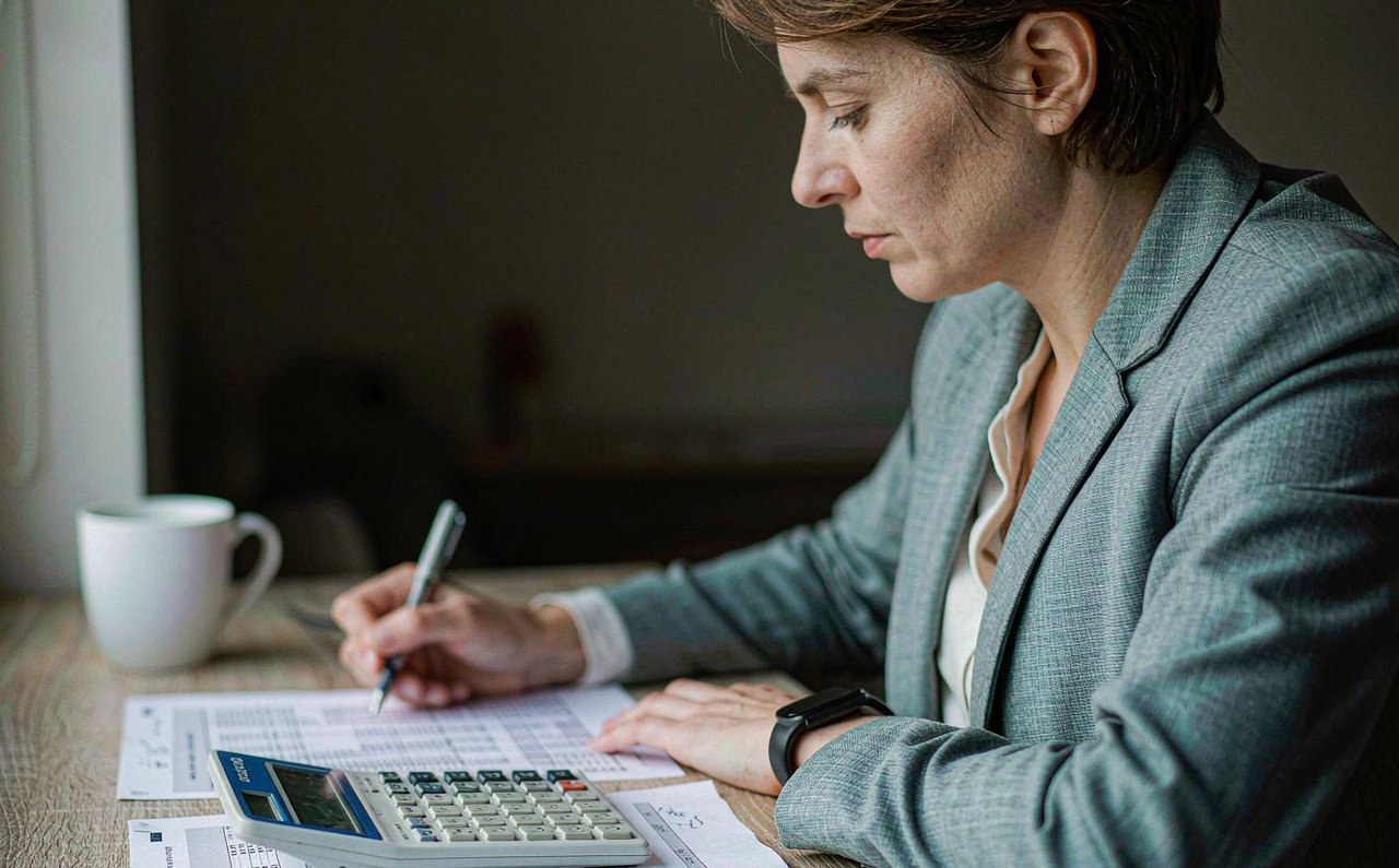 A person reviewing paper tax forms with a calculator at a kitchen table
